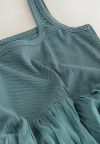 Nahaufnahme eines türkisfarbenen, gerippten Tanktops mit gerafftem, strukturiertem Rockdetail an der Taille vor hellem Hintergrund.