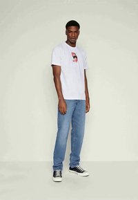 Hvit bomulls T-skjorte med grafisk trykk, kombinert med lys blå denimjeans og svarte sneakers med hvite såler. Rett snitt.