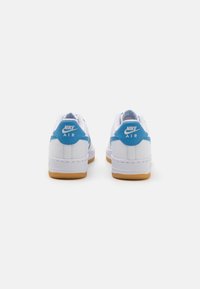 White Nike Air shoes with blue accents, featuring a smooth leather upper, round toe, and gum rubber outsole. Logo on heel and side.