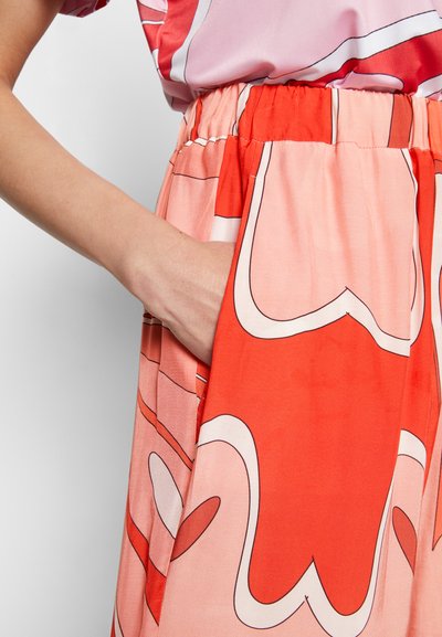 Saia fluída em vermelho vibrante com padrões abstratos em rosa e branco. Apresenta uma cintura elástica e um bolso lateral para conveniência.