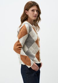 Cardigan en tricot avec un motif argyle en orange, gris et blanc, col en V, manches longues et fermeture à boutons sur le devant. Tissu texturé.