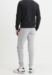 Pantalones de chándal grises con un ajuste slim, combinados con un sudadera oscura. Presentan puños acanalados y una textura suave. Zapatillas con acentos multicolores.