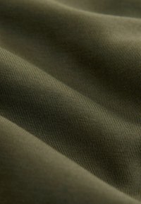 Materiał bawełniany w kolorze oliwkowym o delikatnej, prążkowanej strukturze, prezentujący gładkie, falujące fałdy oraz miękkie, matowe wykończenie.