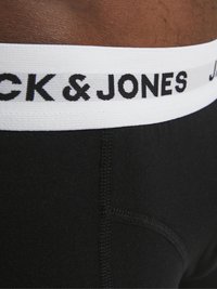 Crne gaće s širokim bijelim elastičnim pojasom na kojem je crnim slovima ispisano "JACK & JONES". Glatka tekstura, uski kroj.