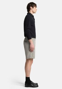 Polo shirt noir à manches longues, shorts gris clair et mocassins noirs avec des chaussettes. Silhouette décontractée et coupe relaxée, sans motifs ni accents visibles.
