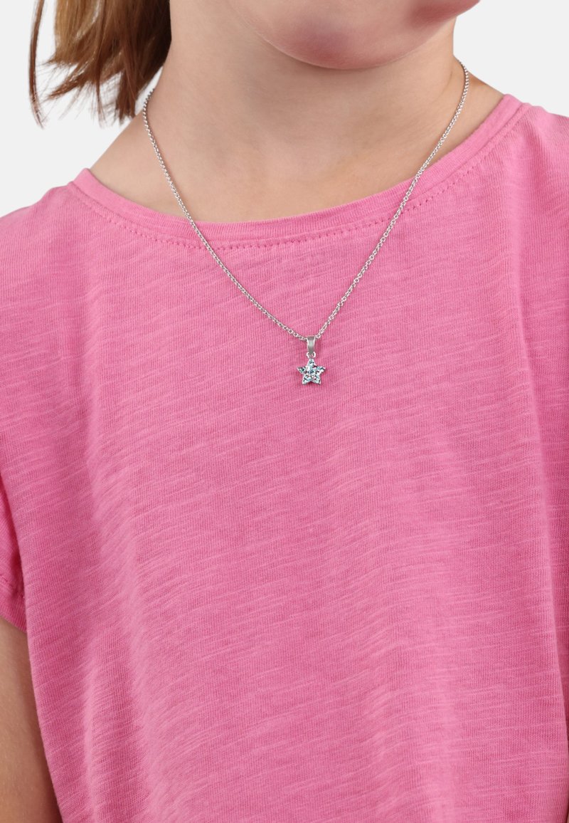 Collana a forma di stella argentata con un accento blu, indossata sopra una maglietta rosa e testurizzata. La catena è delicata e presenta una chiusura semplice.