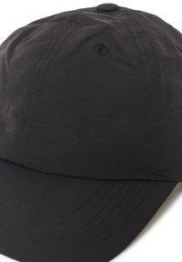 Casquette noire en tissu léger. Elle présente une visière incurvée, des coutures décoratives et un bouton central sur le dessus. Texture lisse avec des lignes verticales.