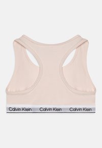 Bežový športový top s prekríženými ramienkami. Obsahuje biely pruh s textom "Calvin Klein" a hladký, elastický materiál.