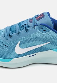 Zapatilla deportiva de color azul claro con parte superior de malla, logo de swoosh blanco, detalles texturizados y suela acolchada con la marca "AIR".