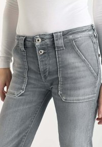 Jeans en denim gris au design ajusté, comprenant deux poches avant, deux poches arrière, et une fermeture à double bouton au niveau de la taille.