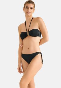 Zwart bikini set bestaande uit een bandeau-top met een gouden accent en verstelbare strikjes aan de onderkant. Flemhuidige textuur en eenvoudig ontwerp.