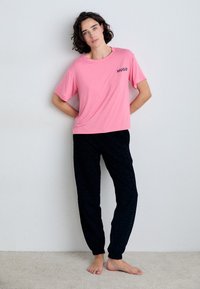 Pink short-sleeve t-shirt with "HUGO" logo, paired with black patterned jogger pants. The outfit has a relaxed fit and is made from soft fabric.
