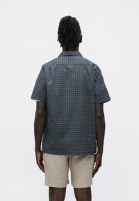 Donkerblauw overhemd met korte mouwen en een geometrisch wit zigzagpatroon. Ontworpen met een kraag en een rechte achterkant. Gecombineerd met lichtbeige shorts.