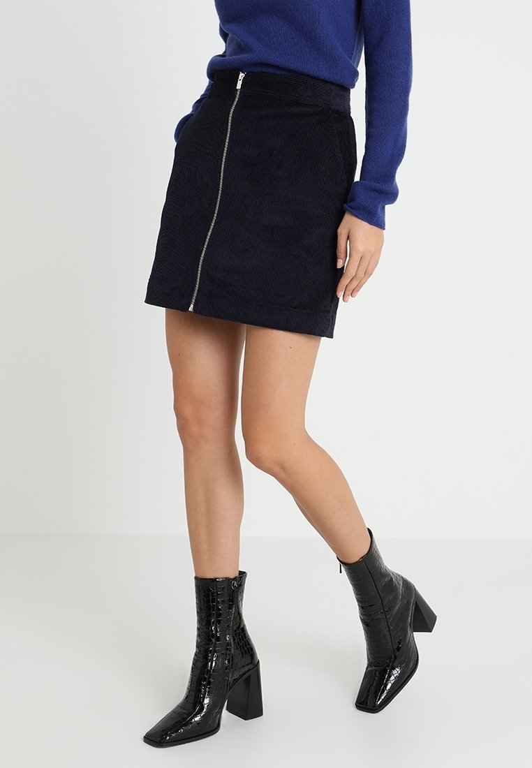 Mini-jupe en velours côtelé bleu marine avec une fermeture éclair à l'avant et une coupe droite. Associée à des bottines noires texturées à talon carré.