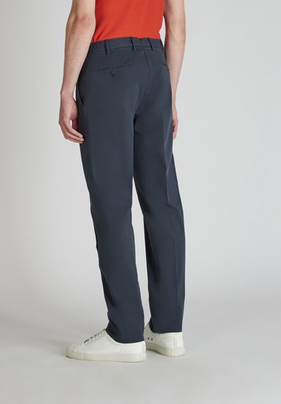 Pantaloni blu navy con una texture liscia, design a gamba dritta, passanti per cintura e una tasca posteriore con bottone. Abbinati a sneakers bianche.