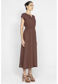 Brązowa, bezrękawnikowa sukienka do kolan z dekoltem w kształcie litery V i elastyczną talią. Zestawiona z sandałami na platformie z przezroczystymi paskami i brązowymi podeszwami.