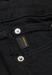 Czarne dżinsy z denimu ze srebrnymi dodatkami, z bliskim ujęciem markowej etykiety i detali szwów.