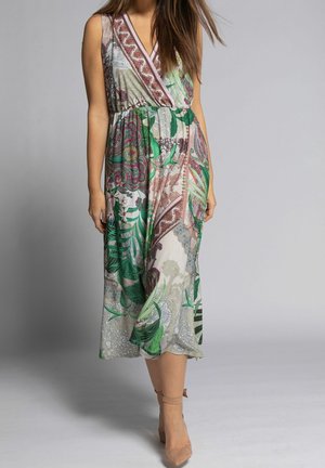 Kobieta w bezrękawną sukienkę midi z dekoltem w serek, zdobioną kolorowymi kwiatowymi i paisley wzorami, nosząca beżowe szpilki z wiązaniem przy kostce, idzie do przodu.