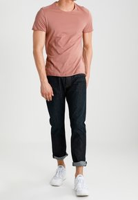 T-shirt rosa chiaro a maniche corte abbinato a jeans blu scuro a gamba dritta e sneakers bianche, che mostrano un look casual e comodo.