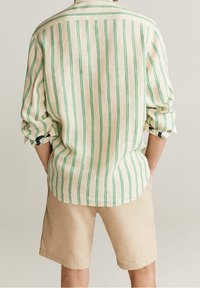 Hellbeige Langarmhemd mit vertikalen grünen Streifen und aufgekrempelten Ärmeln, kombiniert mit beigen Shorts.