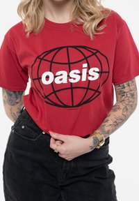 Red cotton t-shirt featuring a large black globe graphic with the word "oasis" in white. Pairing with black high-waisted jeans.