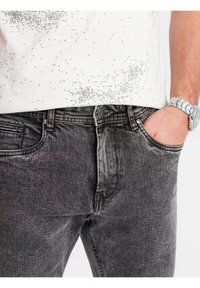 Jean en denim gris avec une légère texture délavée, design à cinq poches et fermeture éclair. Le tissu semble doux et usé.