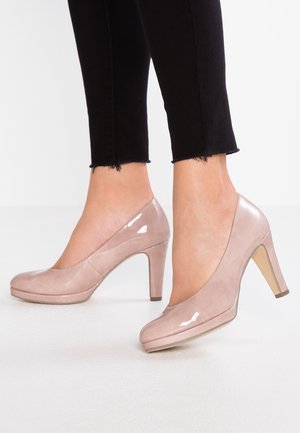 Beige lakleren hoge hakken met een ronde neus en een blokhak van 10 cm, gecombineerd met zwarte cropped skinny jeans. Gladde textuur met een glanzende afwerking.