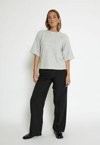 Light gray knit sweater with wide short sleeves, worn with black wide-leg trousers and shiny black shoes. Relaxed fit, soft texture.