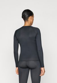 Zwarte sportieve top met lange mouwen, een strakke pasvorm, gladde textuur en platte naden, gecombineerd met bijpassende strakke broek.