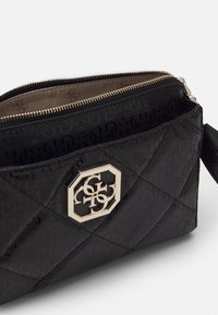 Sort quiltet håndtaske med en blank overflade, der har et gyldent sekskantet logo, en lynlåsfindning og et beige interiør med et logomønster.