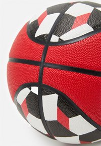 Red and black basketball with textured surface, featuring a geometric pattern of triangles in red, black, and white, with black rubber accents.