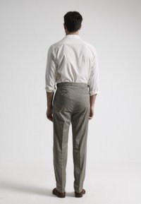 Pantalones en gris claro para hombre con bolsillos laterales y bolsillos traseros con botón, combinados con una camisa blanca. Tela suave y transpirable, corte a medida.