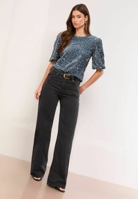 Ziliem dūmaka ar īsām pūkām, saskaņota ar augsto vidukli melniem platajiem džinsiem un melnu jostu. Gluda tekstūra un pieguļošs dizains.