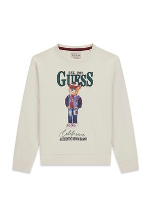 Felpa crema con un orso di cartone che indossa una giacca varsity, un cappello e jeans; il testo recita "GUESS EST. 1981 California Authentic Denim Brand."