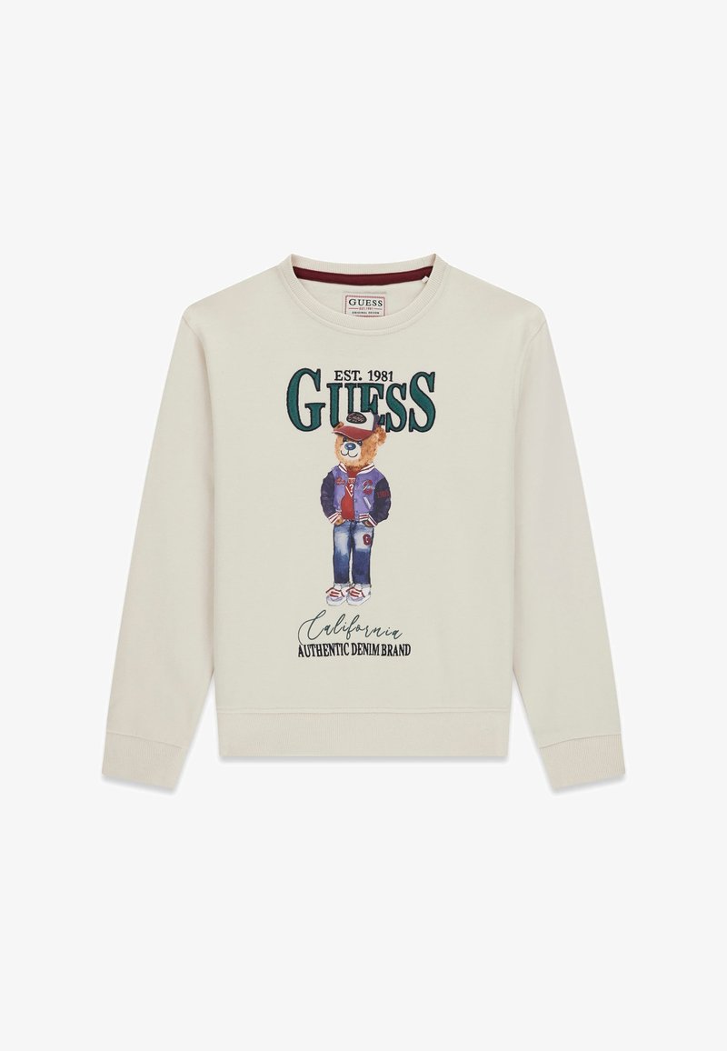 Crème sweatshirt met een cartoonbeer die een varsityjack, pet en jeans draagt; tekst luidt "GUESS EST. 1981 California Authentic Denim Brand."