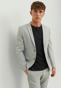 Light gray single-breasted blazer with two buttons, textured fabric, paired with a black crew-neck t-shirt and matching trousers.