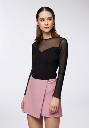 Top nero a maniche lunghe in tessuto trasparente con scollo a cuore, abbinato a una gonnellina avvolgente di un rosa chiaro. Texture morbide e design moderno.
