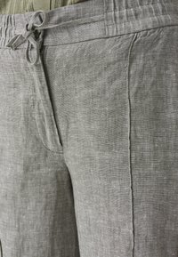 Primo piano di pantaloni in lino grigio chiaro con vita con coulisse e cucitura laterale visibile.