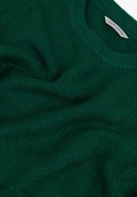 Jersey verde con un suave tejido texturizado, que presenta un escote redondo y una etiqueta con la inscripción "DAN JOHN" en un lazo de tela.