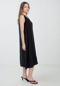 Vestito nero senza maniche realizzato in tessuto leggero, caratterizzato da una vestibilità comoda, lunghezza fino al polpaccio e un design semplice senza ulteriori motivi.