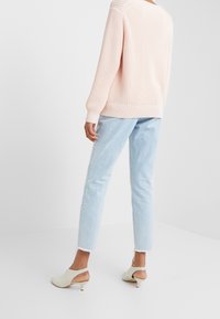 Pull en maille rose clair, jean court bleu clair avec ourlet effiloché, mules à talons ouvertes couleur crème. Accent sur la texture et le contraste des couleurs.