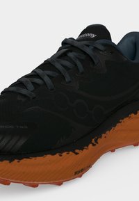 Chaussure de running noire Saucony avec des lacets gris foncé et une semelle orange dotée de la technologie d'amorti PWRRUN.