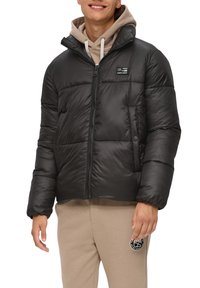 Schwarze Daunenjacke mit Reißverschluss, horizontalen Nähten, hohem Kragen und Logopatch. Trägt man über einem beigen Hoodie und passenden Hosen.