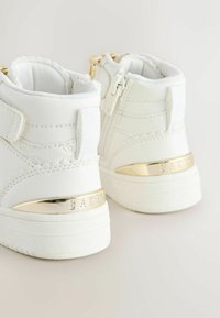 Hvide høj-top sneakers lavet af glat syntetisk materiale. Udstyret med guldfarvet hardware på hælen med "BAKER" indgraveret. Velcro-lukning.