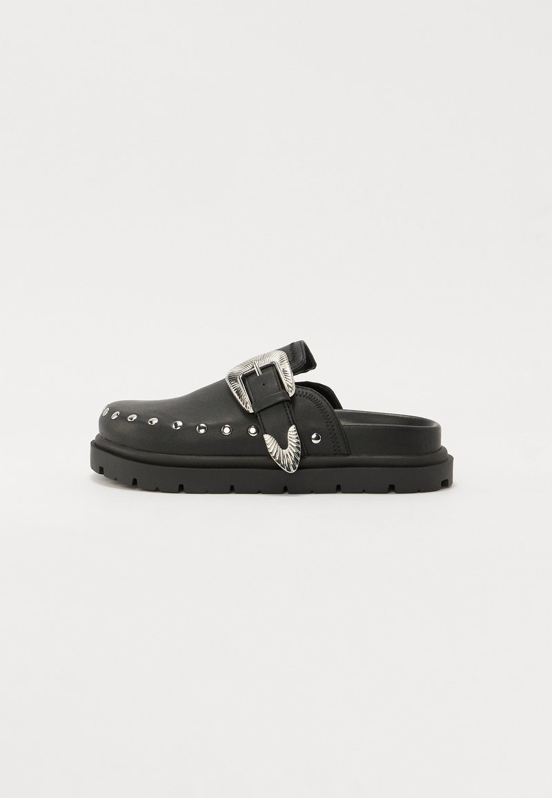 Schwarze Lederclogs mit einer dicken, strukturierten Sohle, silberner dekorativer Schnalle und genoppten Akzenten an der Seite.