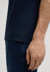 Marineblauwe katoenen t-shirt met een gestructureerde afwerking, voorzien van een klein zwart logo-label aan de zoom, gecombineerd met donkerblauwe denim jeans.