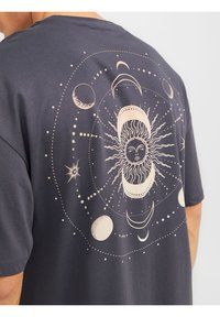 Grafisches T-Shirt aus dunkelgrauer Baumwolle mit einem detaillierten Sonnen- und Monddesign in Beige, umgeben von himmlischen Elementen wie Sternen und Kreisen.