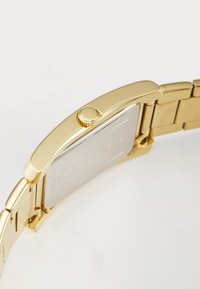 Guldtonet armbåndsur med rektangulær urskive, struktureret krone og metalarmbånd. Bagsiden har en glat sølvfinish.