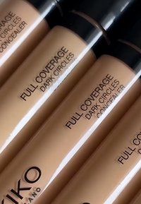 Tubes de correcteur pour cernes à couvrance totale dans un emballage transparent avec des bouchons noirs. Les produits contiennent un liquide teinté beige et arborent des marques imprimées.