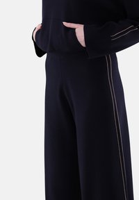 Marinefarbene Jogginghose im entspannten Schnitt, mit vertikalen sandfarbenen Streifen entlang der Seitennähte und einem weichen, strukturierten Stoff.